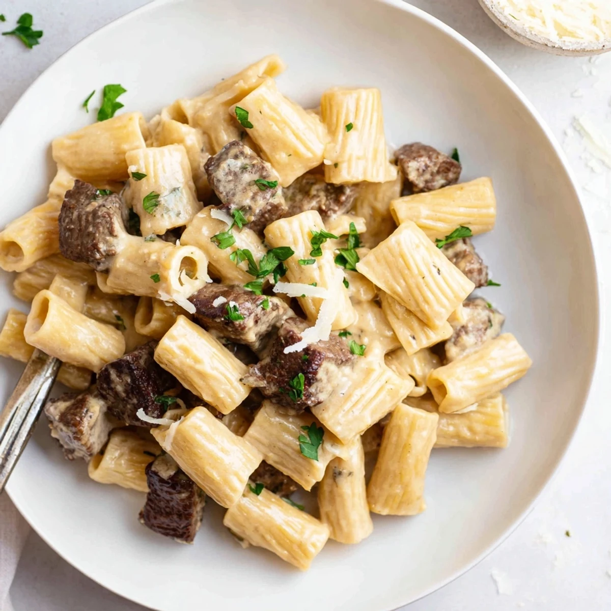 Creamy Garlic Butter Steak Parmesan Rigatoni served in a rustic bowl, garnished with parsley.  