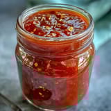 Homemade fermented hot sauce in a glass bottle, showcasing a rich red hue and bold, tangy aroma from chili peppers and garlic.