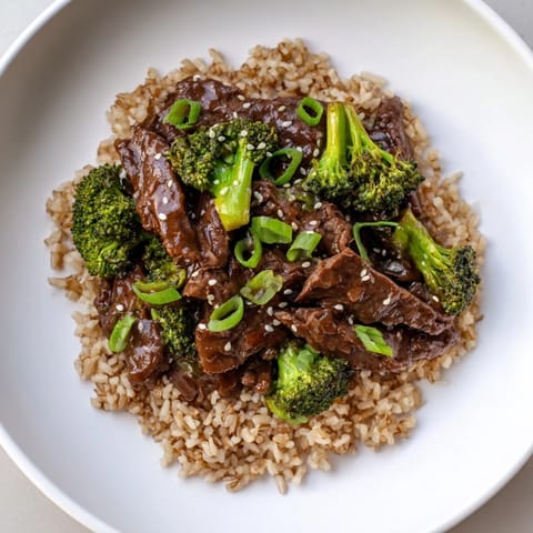 Fluffy brown rice topped with greens and the delicious Slow-Cooker Beef & Broccoli recipe, ready to serve.