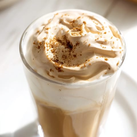 Creamy, cloud-like peaks of whipped Dalgona coffee gracefully float over a tall glass of milk, a simple delight.