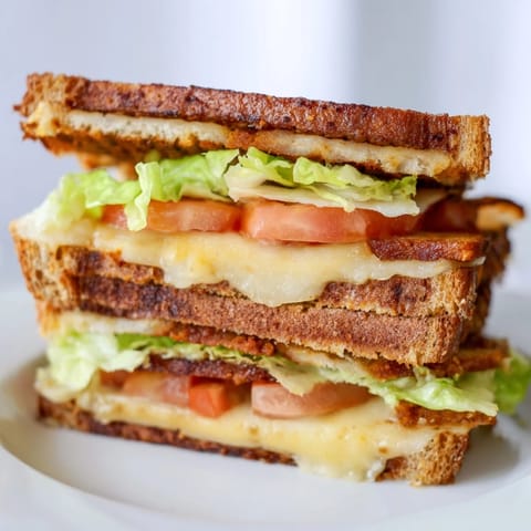 Close-up of a Vegan Bacon BLT Grilled Cheese sandwich on a wooden board, featuring crunchy bread and fresh colorful vegetables.