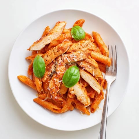 Golden-brown seared chicken strips and penne pasta coated in a vibrant, zesty chili-infused tomato sauce, garnished with fresh basil and Parmesan.