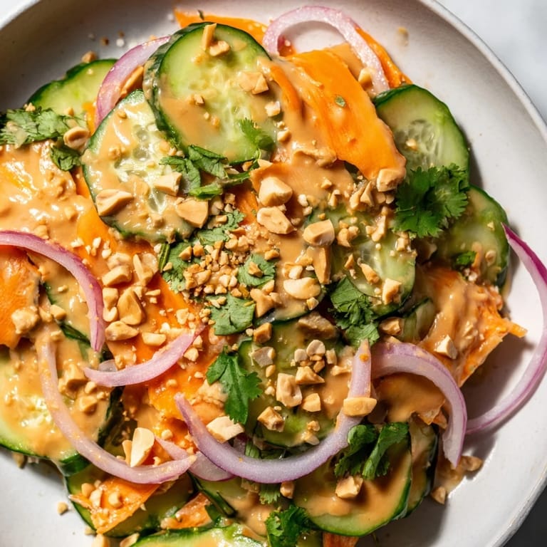 A colorful bowl of Thai-Style Peanut Cucumber Salad featuring shredded carrots and chopped peanuts sprinkled on top.
