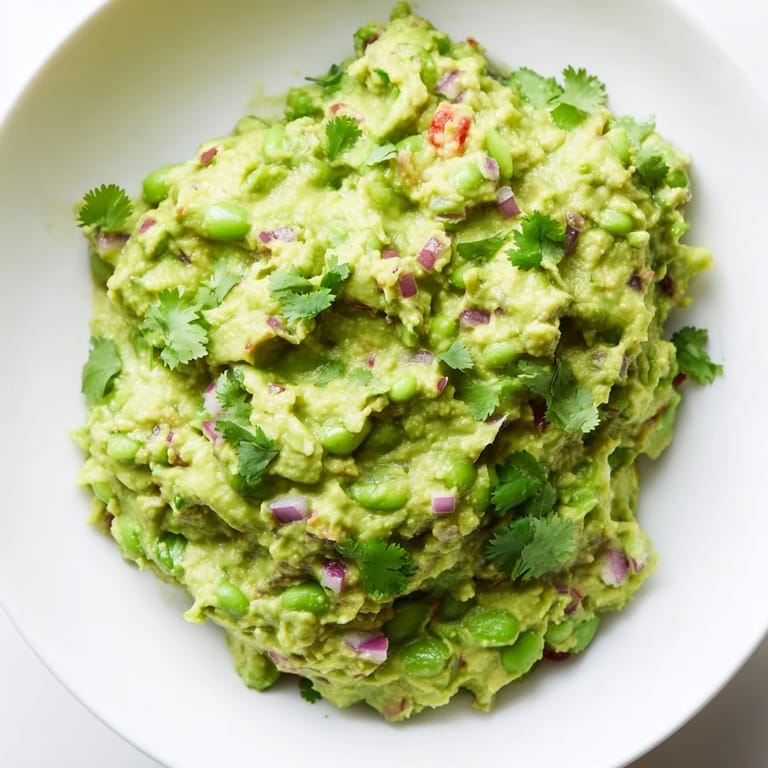 Fresh, homemade Edamame Guacamole with visible chunks of tomato, is ready to be scooped up with chips.