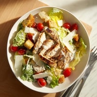 Tender grilled chicken strips lie atop crisp romaine lettuce, drizzled with creamy Greek yogurt Caesar dressing.  